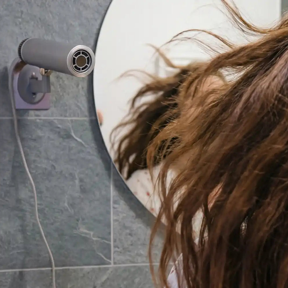 Person with long brown hair using a hair dryer in a bathroom setting.